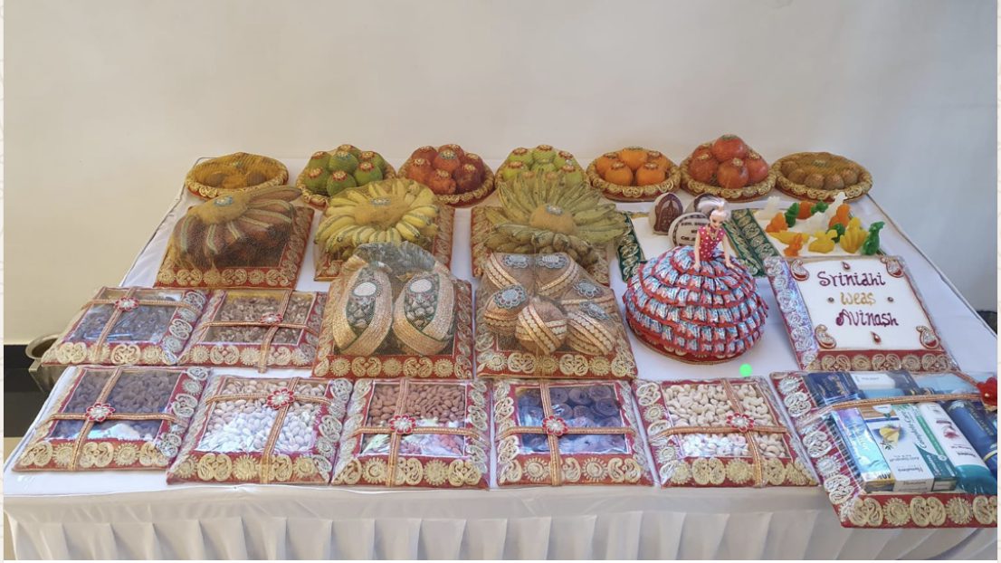 Nichayathartham display of fruit, dry fruit, sweets, and trays on a long table.